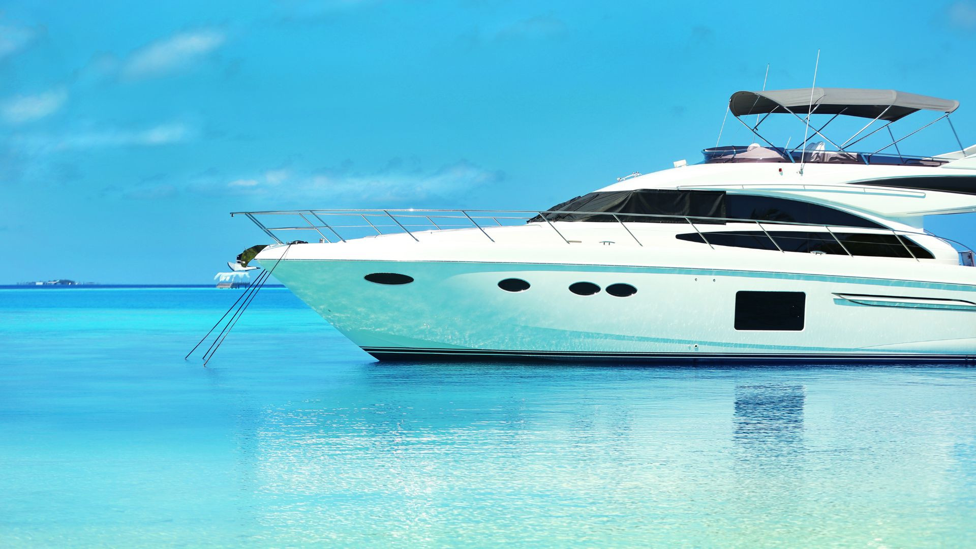 A white luxury yacht is anchored in clear, calm blue water near Marina Flamingo, basking under a bright, sunny sky.